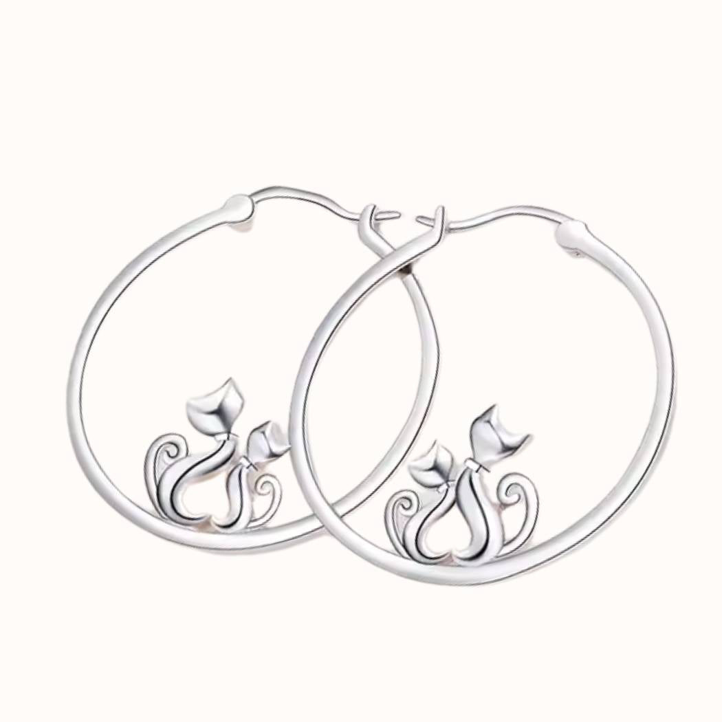 Pendientes de plata con forma de aro con 2 gatos que hacen un corazón con el cuerpo, sobre fondo beige de TOUS