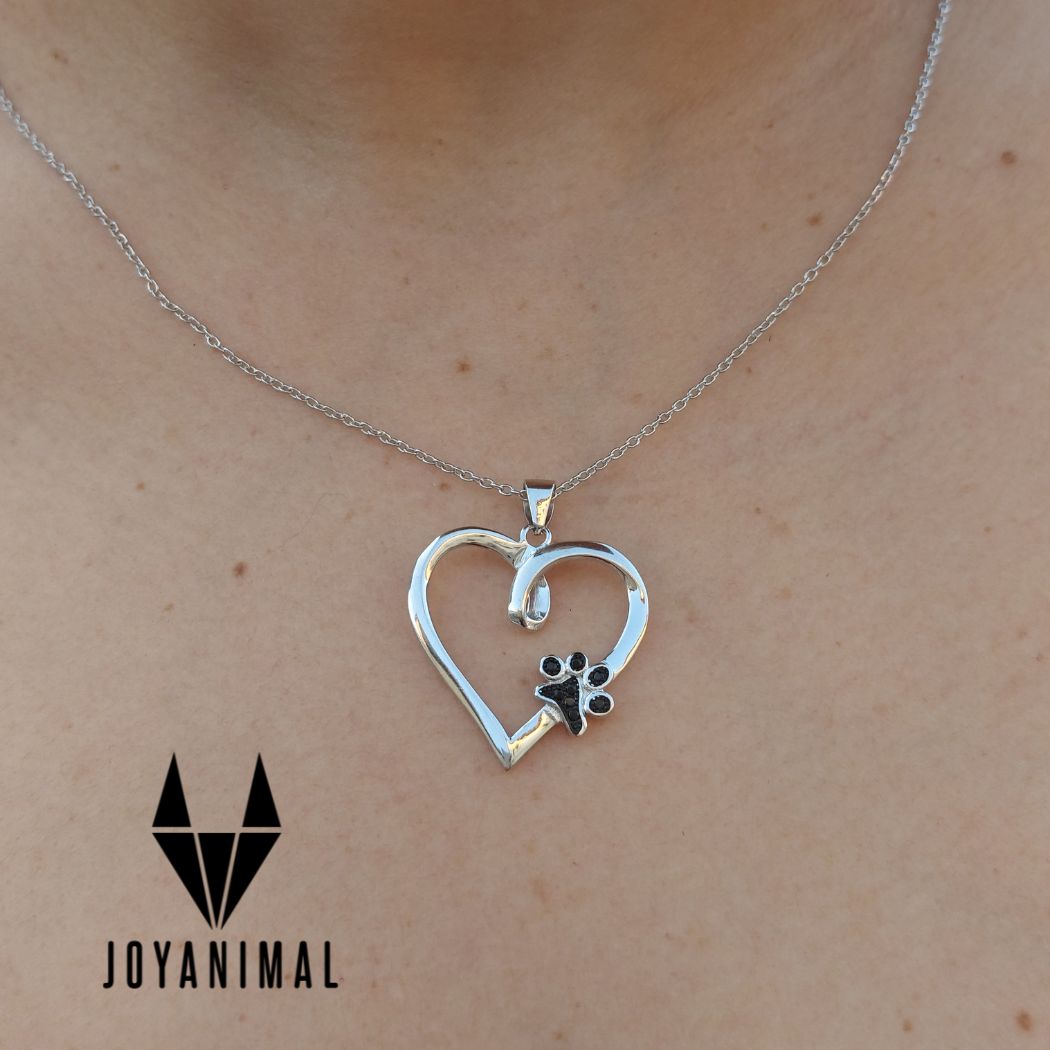 Gargantilla con cadenita fina de plata, sobre cuello de modelo mujer y con colgante con un corazón y una huellita negra, sobre cuello de mujer modelo, del corte inglés