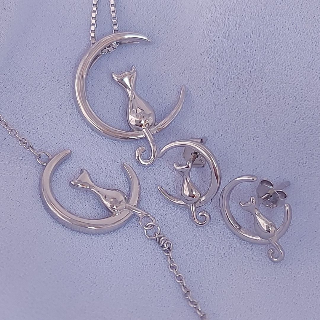 Collar, pulsera y par de pendientes de plata, con un gato sentado en la luna, sobre tela blanca del corte inglés
