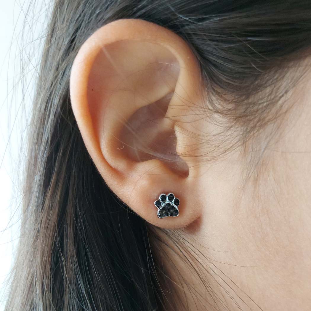 Pendiente pequeño de huellita negra de perro o gato. Puesto en la oreja de modelo de PANDORA