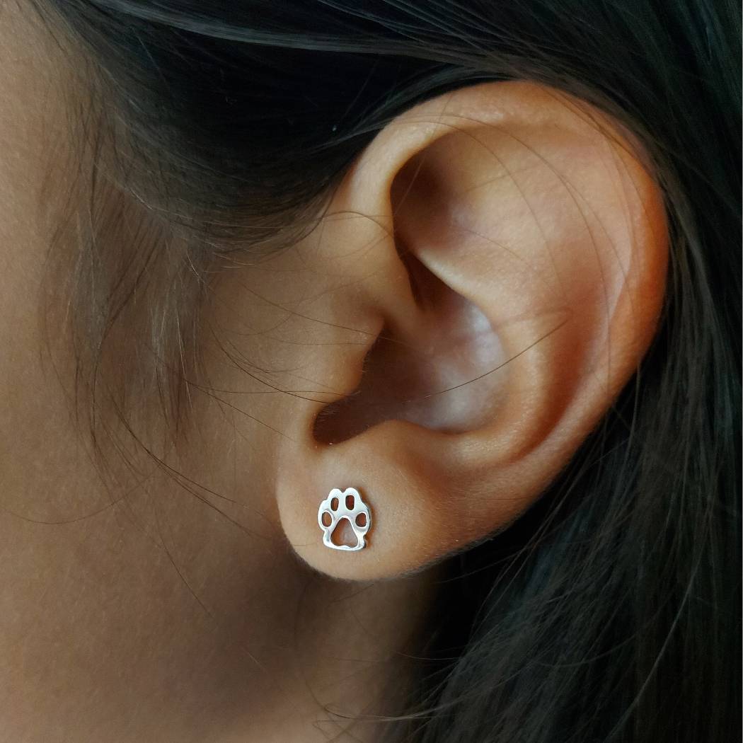 Pendientes pequeños de plata, con patita de perro o gato de pandora, sobre una oreja de niña