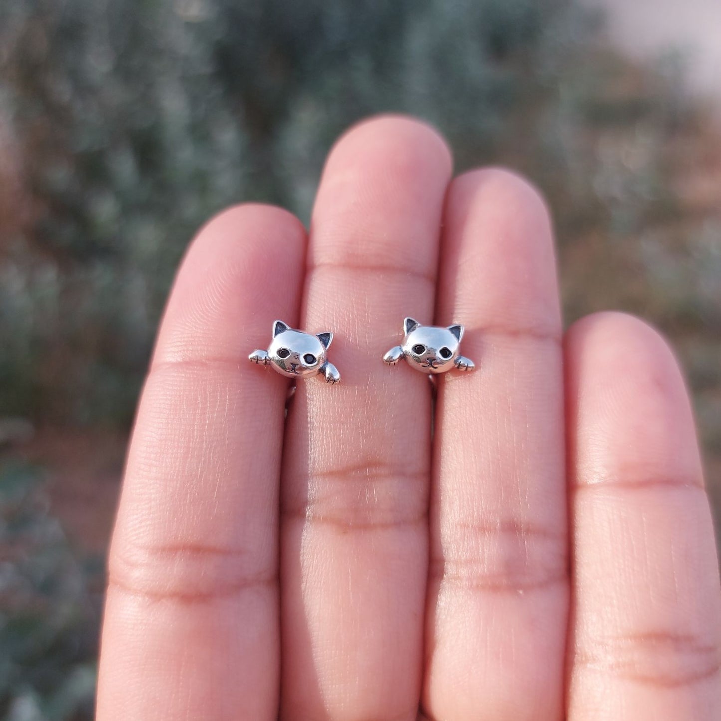 Pendientes de plata en mano de mujer con forma de cabeza y patas de gatito de TOUS