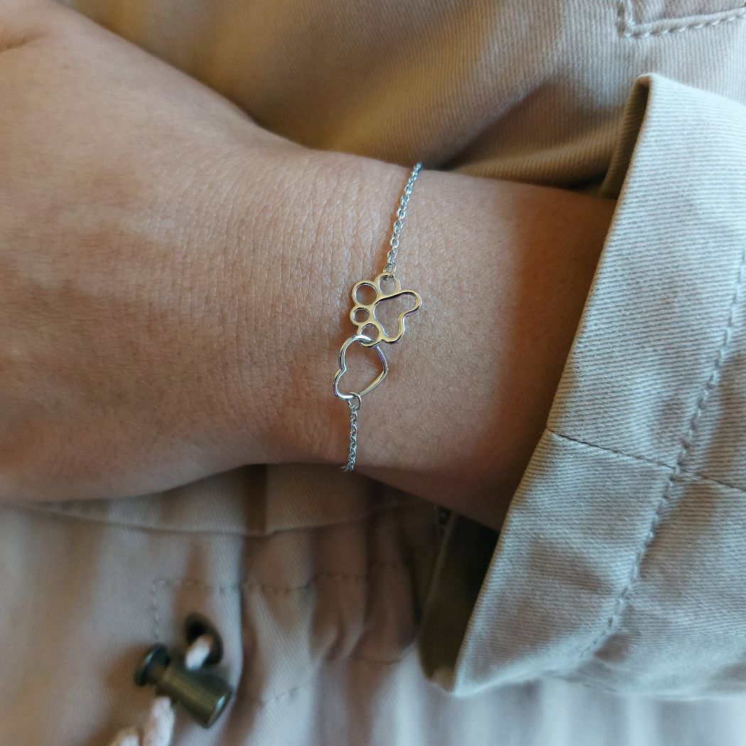 Pulsera con un corazón y una huella de perro o gato, de plata puesta en una muñeca de mujer con gabardina gris de el corte inglés