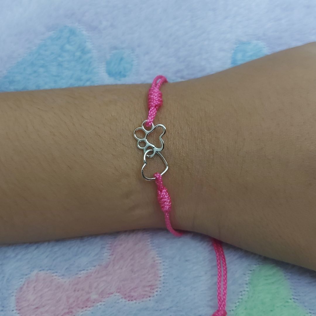 Pulsera con nudos ajustables de hilo rosa, con un corazón y una pata de perro de pandora
