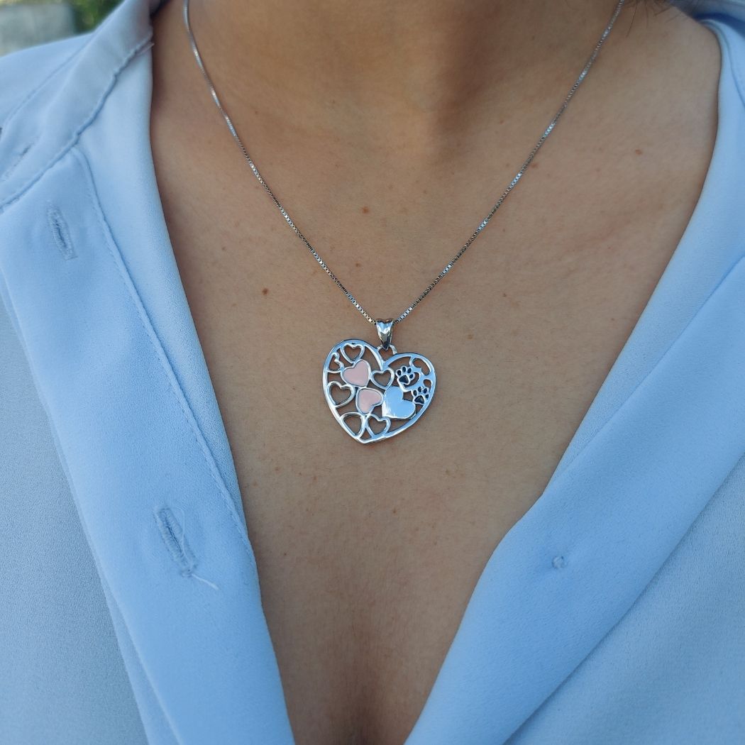 Colgante de árbol de vida con cadena de plata con corazones rosas y huellitas sobre camisa azul en modelo de pandora