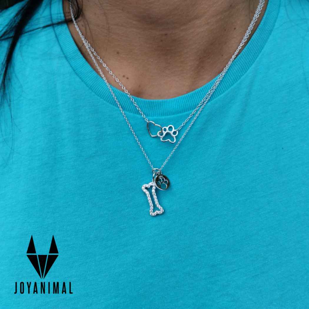 Gargantilla y collar de plata con formas de huellas y huesos de perrito en el cuello de una modelo mujer sobre con camiseta azul de Tous.