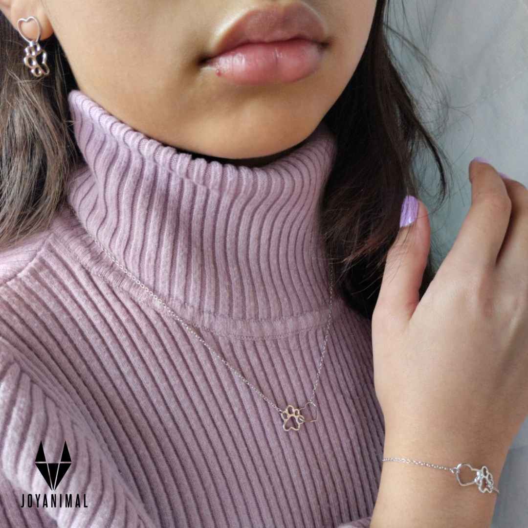 Hermosa chica con pulsera, collar y pendientes de plata, con formas de huellas de perritos o gatitos , puestos con jersey morado de el corte inglés