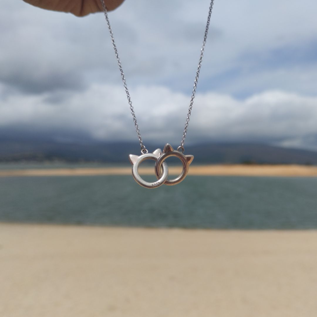 Collar de pareja de gatitos en oro y plata sujetándolo una mujer en la playa, de el corte inglés