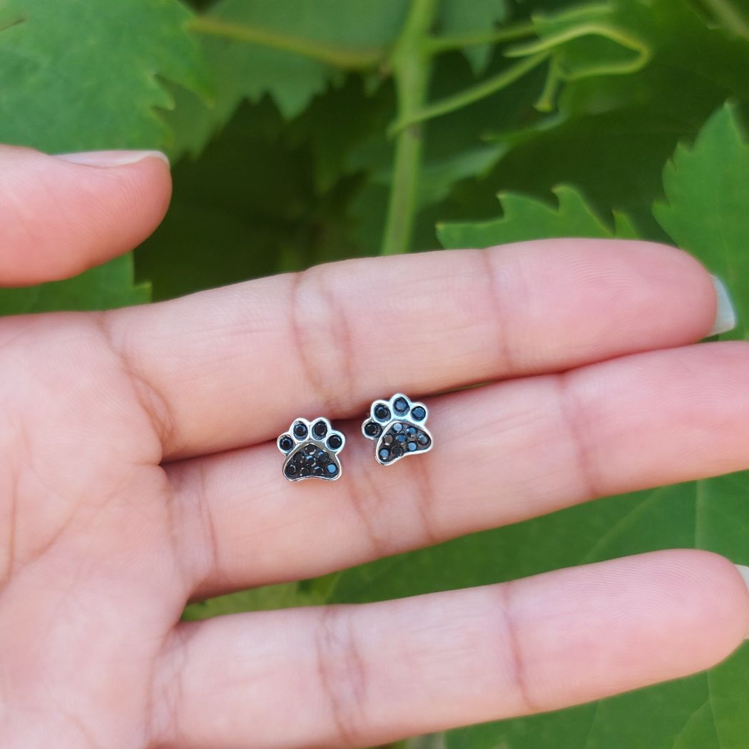 Pendientes de pata de perro o gato, con zirconita negra puestos en mano de JOYANIMAL