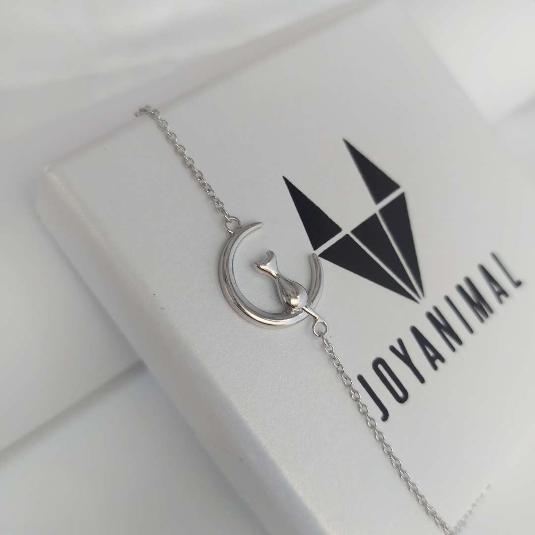 Pulsera de plata con una luna con un gato sentado en ella, sobre una caja de regalo del corte inglés