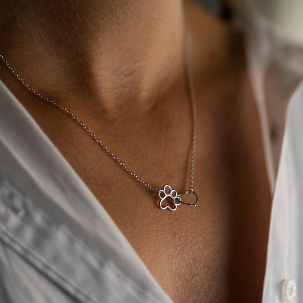 Gargantilla puesto en el cuello de una mujer, con cadena fina y colgante con forma de pata y corazón de perrito o gatito de tous