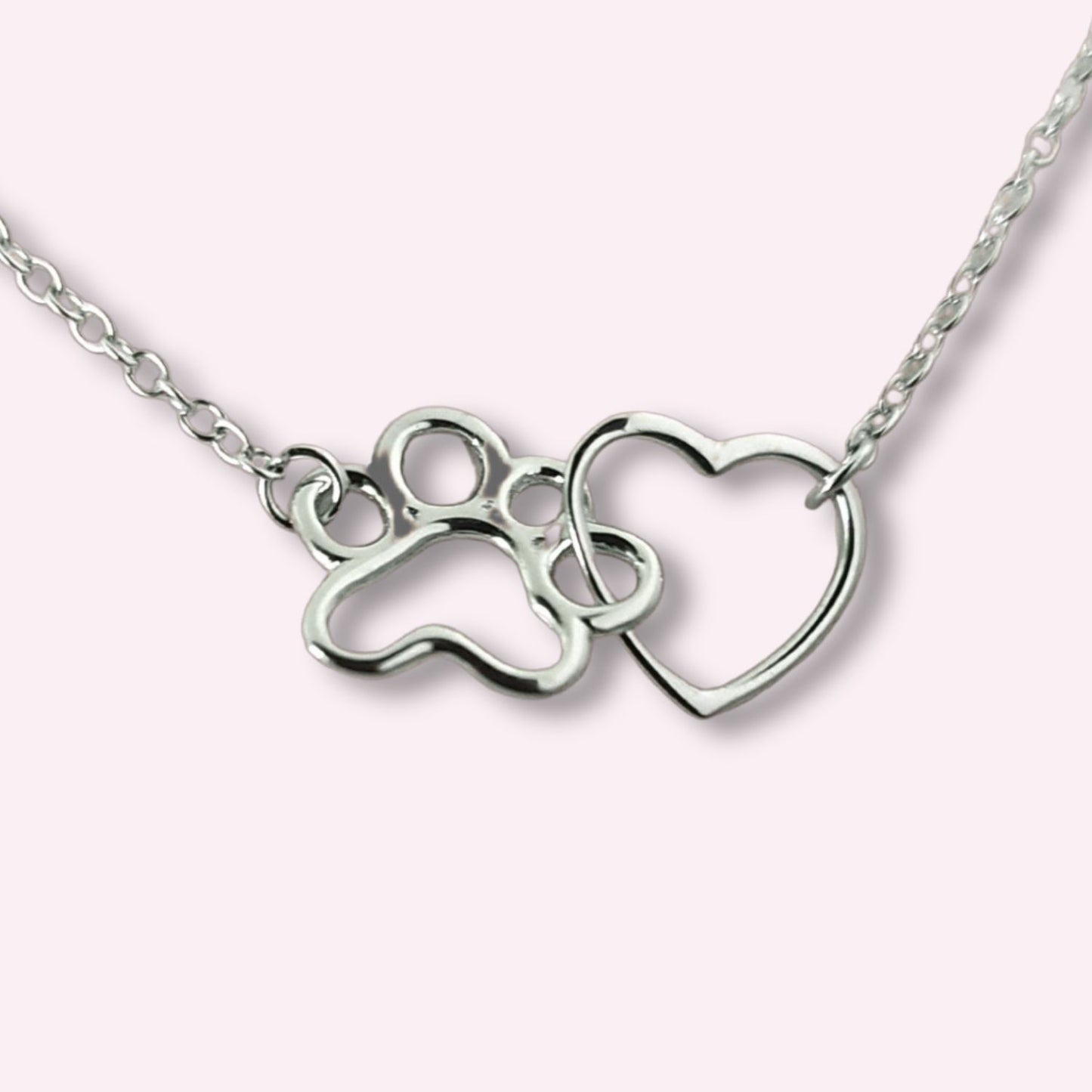 Colgante con corazón y huellita de perrito o gatito en plata de ley sobre un fondo rosa de TOUS