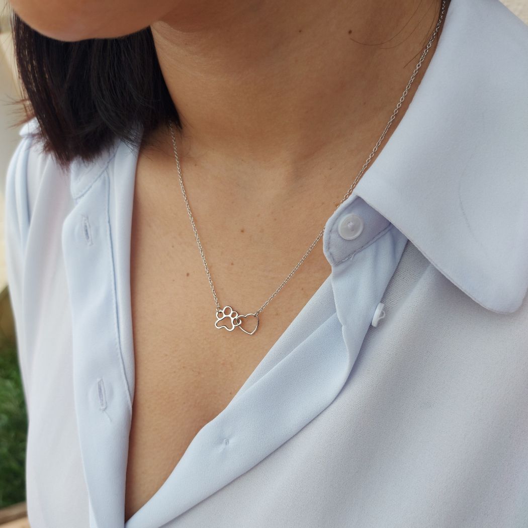 Collar con una huella y un corazón de plata de ley by Pandora, sobre una tela rosa