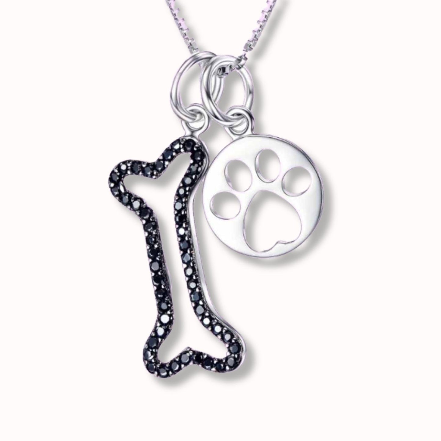Colgantes de huellita de perro con hueso con piedras negras de swarovski sobre fondo rosa