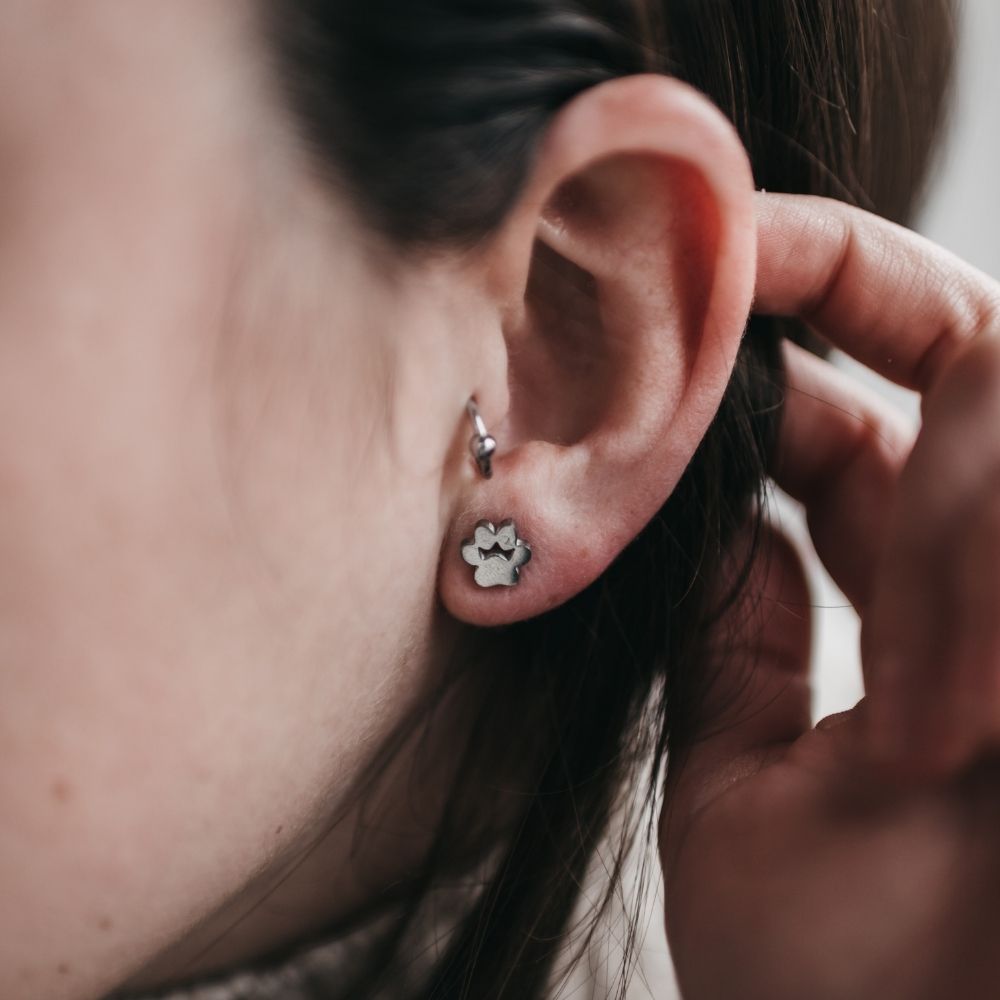 Pendiente con forma de huellita de animal puesto en la oreja junto con un arete de singularu