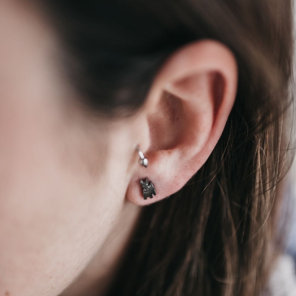 Pendiente pequeño con forma de perrito terrier de mujer junto a arete de PANDORA en segundo agujero.