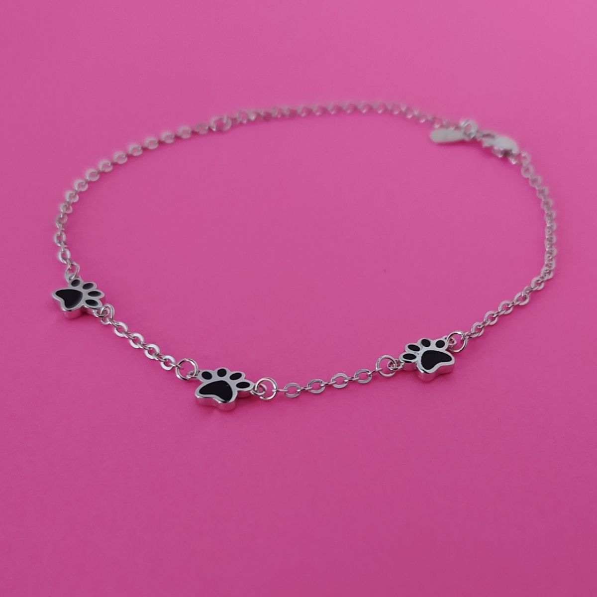 Pulsera de plata con huellas negras para amantes de macotas sobre fondo rosa de PANDORA