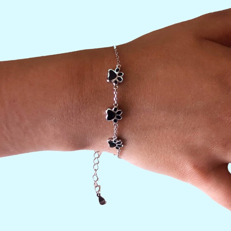 Pulsera de plata con huellitas negras de perro o gato. Sobre muñeca de modelo de TOUS