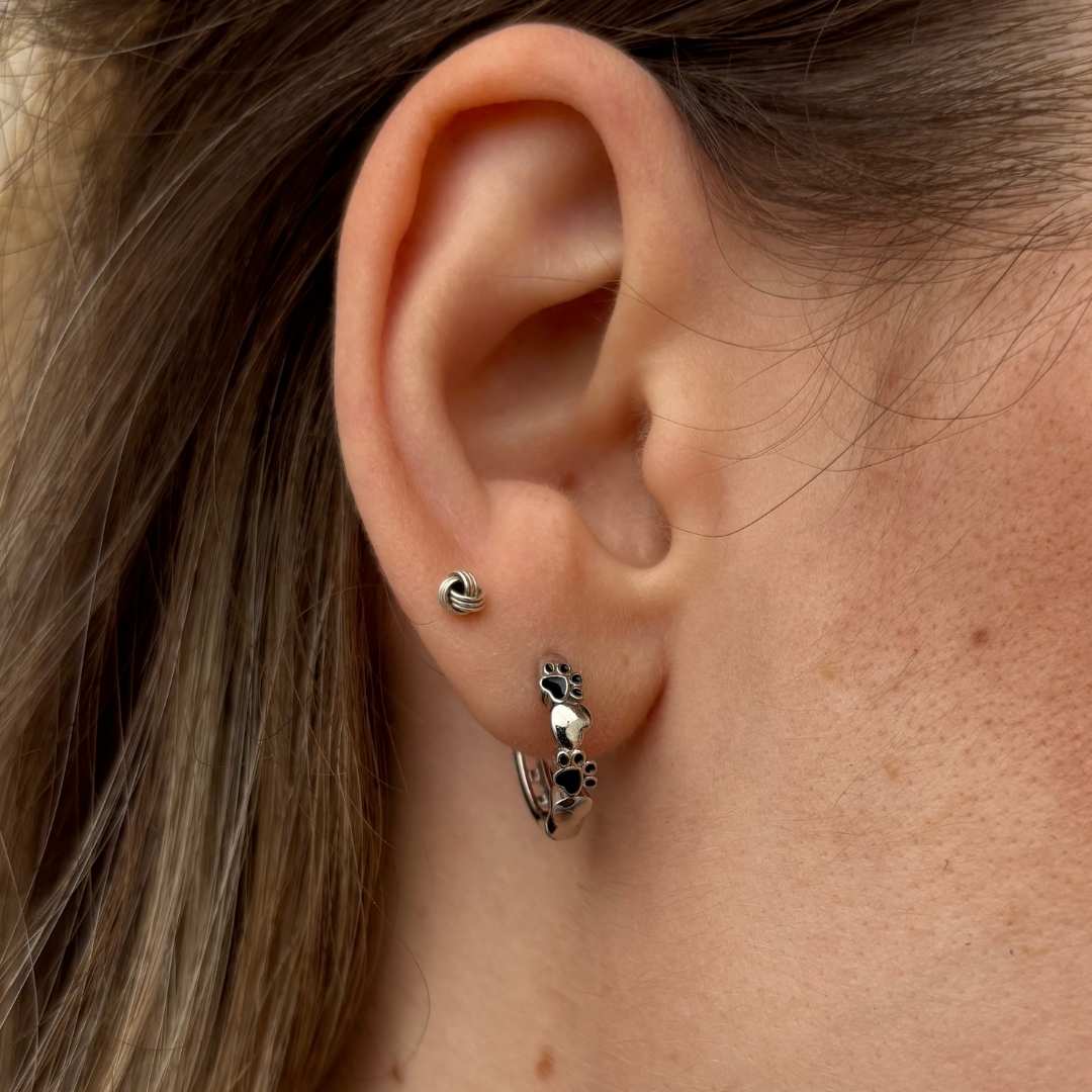 Aretes pequeños con huellas negras y corazón, en oreja de mujer modelo de TOUS