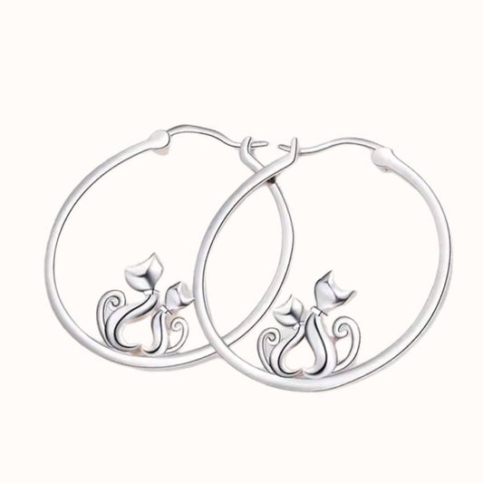 Pendientes de plata con forma de aro con 2 gatos que hacen un corazón con el cuerpo, sobre fondo beige de TOUS