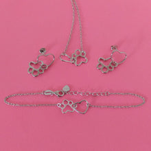 Conjunto de  pulsera, collar y pendientes de plata brillante con colgantes de corazón y huella sobre fondo rosa 