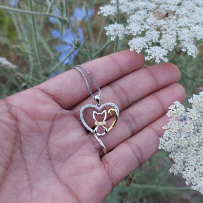 Collar con colgante de corazón con gato que lleva corbata en plata y oro, en mano de modelo PANDORA