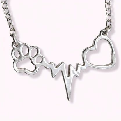 Collar con latidos, una huellita de mascota y un corazón, de plata, sobre fondo rosa pálido de TOUS