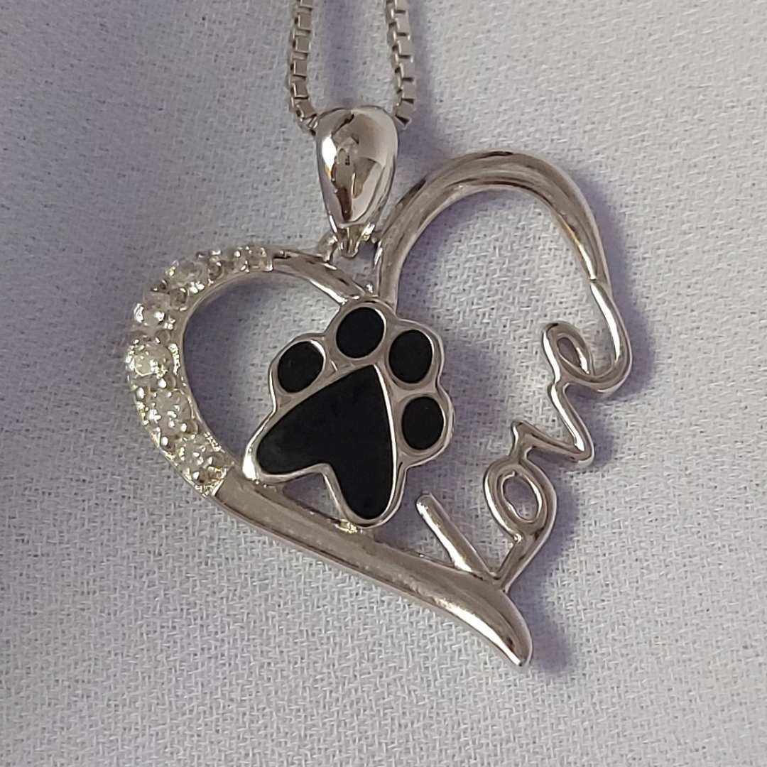 Collar para honrar a los perros o gatos, formado por una huella negra, dentro de un corazón con brillantes y la palabra love, sobre un mantel blanco del corte inglés