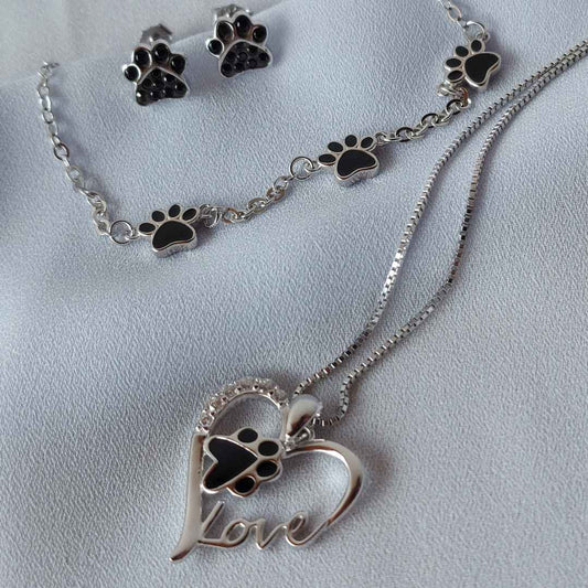 Conjunto de joyas en plata con huellas negras de perros o gatos. Y tiene un diseño con un corazón con una huella negra en el interior, y en el contorno unos brillantes blancos y la palabra love tallada. La pulsera tiene 3 huellitas negras. Presentadas en una bonita caja con forma de bolsa con asas para regalo.By PANDORA