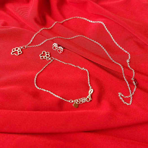 Cadenas de plata de pulsera y collar, junto a pendientes, todos los detalles con huellitas de animales, sobre una tele roja, TOUS