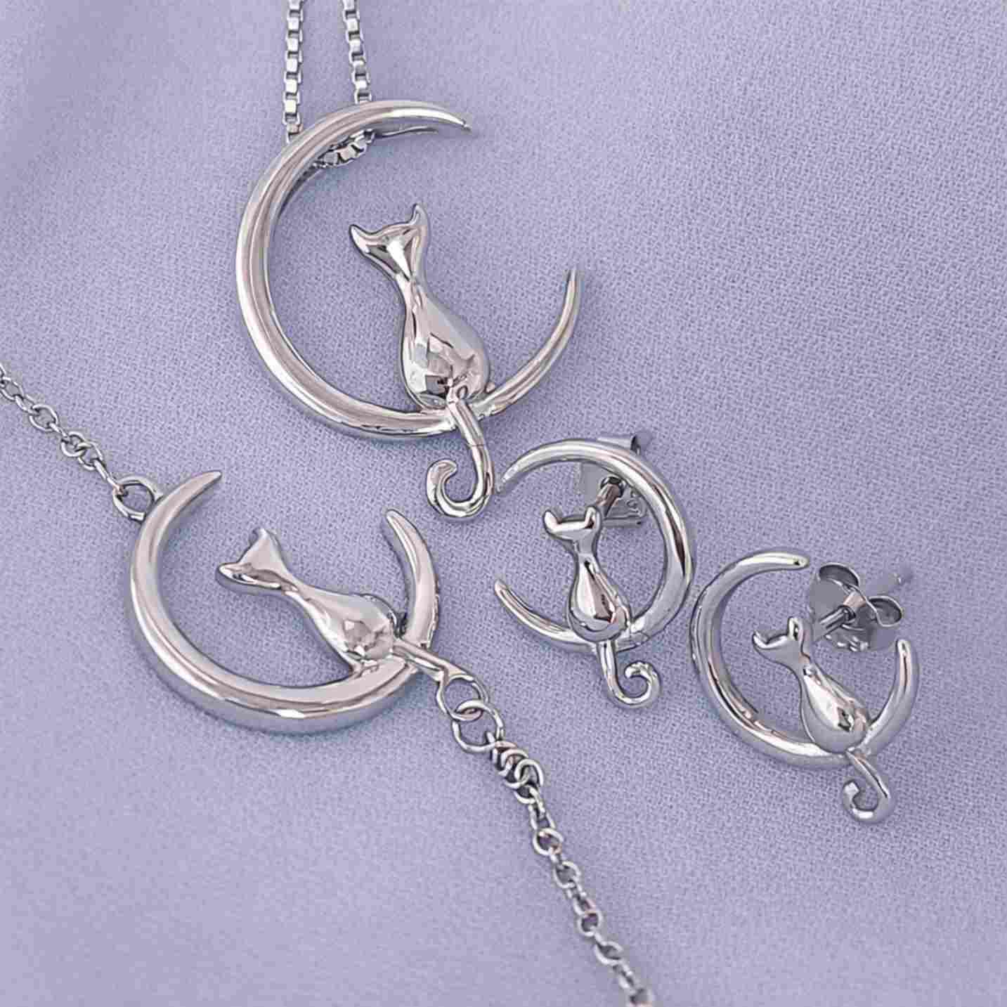 Collar, pulsera y par de pendientes de plata, con un gato sentado en la luna, sobre tela blanca del corte inglés
