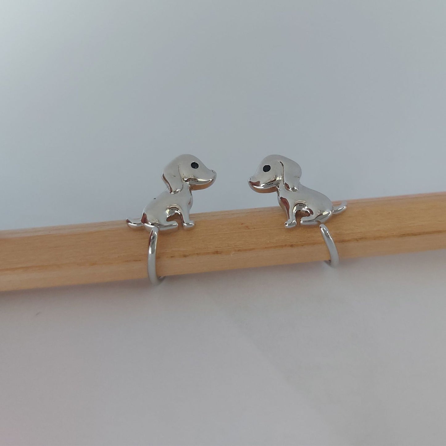 Pendientes de plata con forma de perrito con la cola enrollada sobre un lapiz de madera