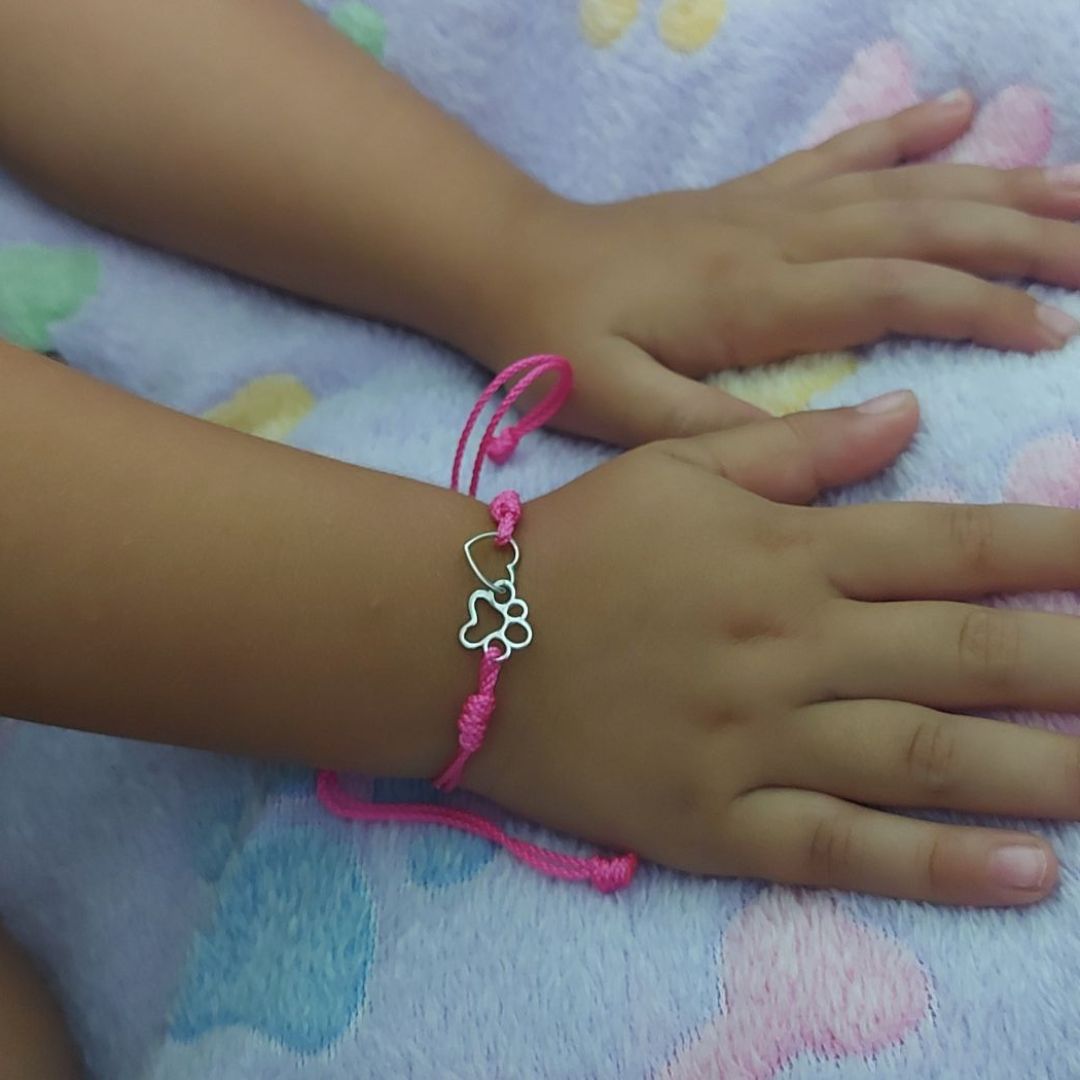 Manitas de niña  con una pulsera rosa, ajustable, con un corazón y una huella de perro o gato, sobre una manta de huellas y huesos de el corte inglés