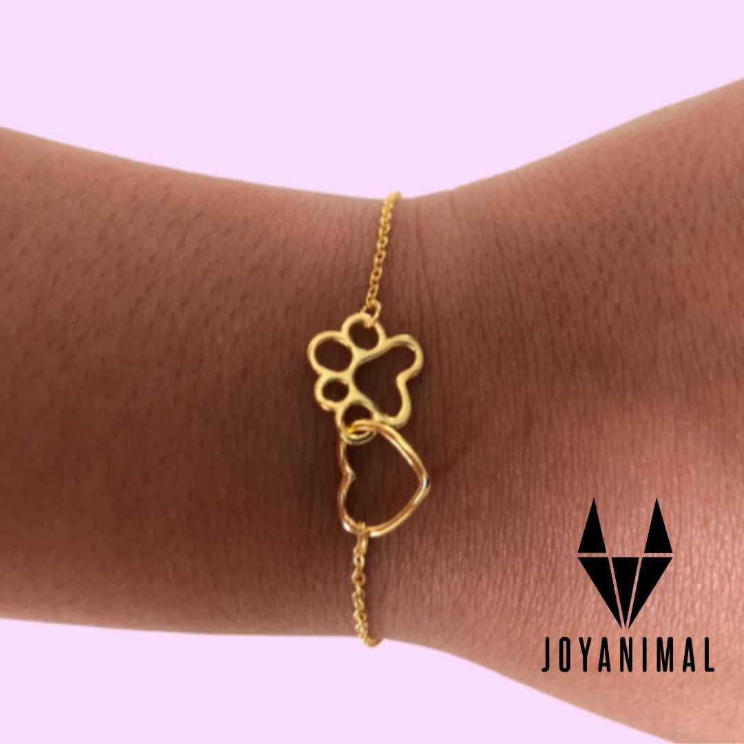 Pulsera de plata bañada en oro con forma de huella y corazón sobre una muñeca de mujer