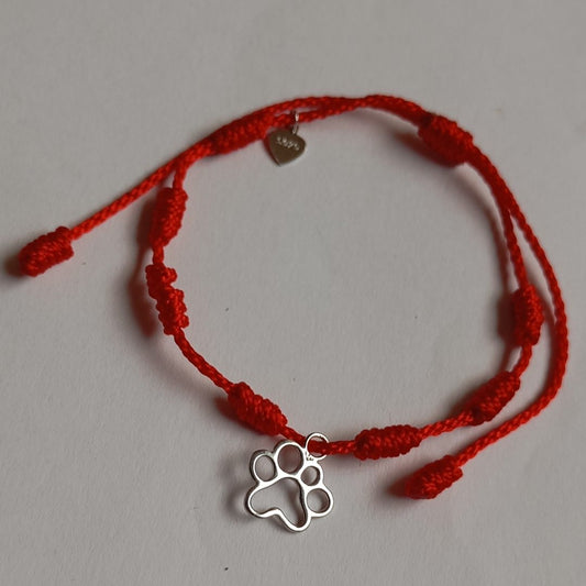 Pulsera de la suerte con 7 nudos de hilo rojo, con detalle de plata con huellas de mascota, sobre manta de el corte ingles