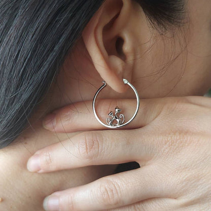 Pendientes de plata con forma de aro con 2 gatos de PANDORA en oreja de mujer con una mano debajo
