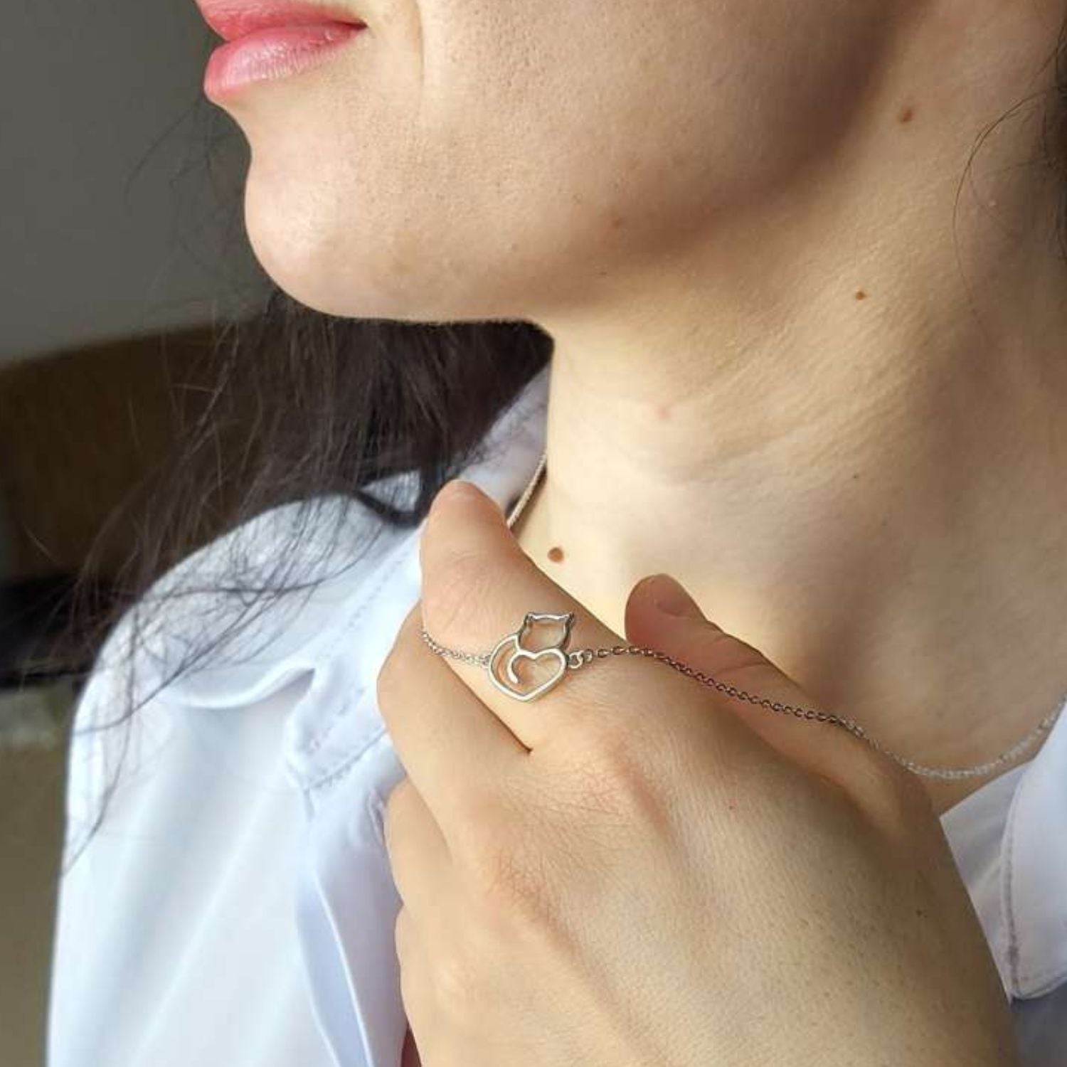 Collar de plata con un gato y corazón sobre mano de modelo con camisa azul del corte inglés