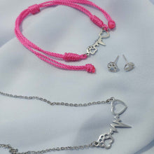 Collar con latido, corazón y huella de mascota, pulsera de hilo rosa con el mismo diseño y pendientes de plata de huellitas, sobre una tela de seda gris, para regalo de comunión del corte ingles