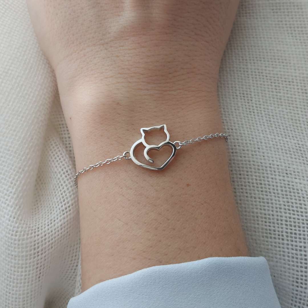 Pulsera en la muñeca de una mujer con la silueta de un gato con un corazón de plata de 925 sobre tela blanca