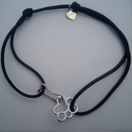 Pulsera con adorno de huella de perro y hueso, de hilo negro e hilos ajustables. Sobre fondo blanco, de Pandora