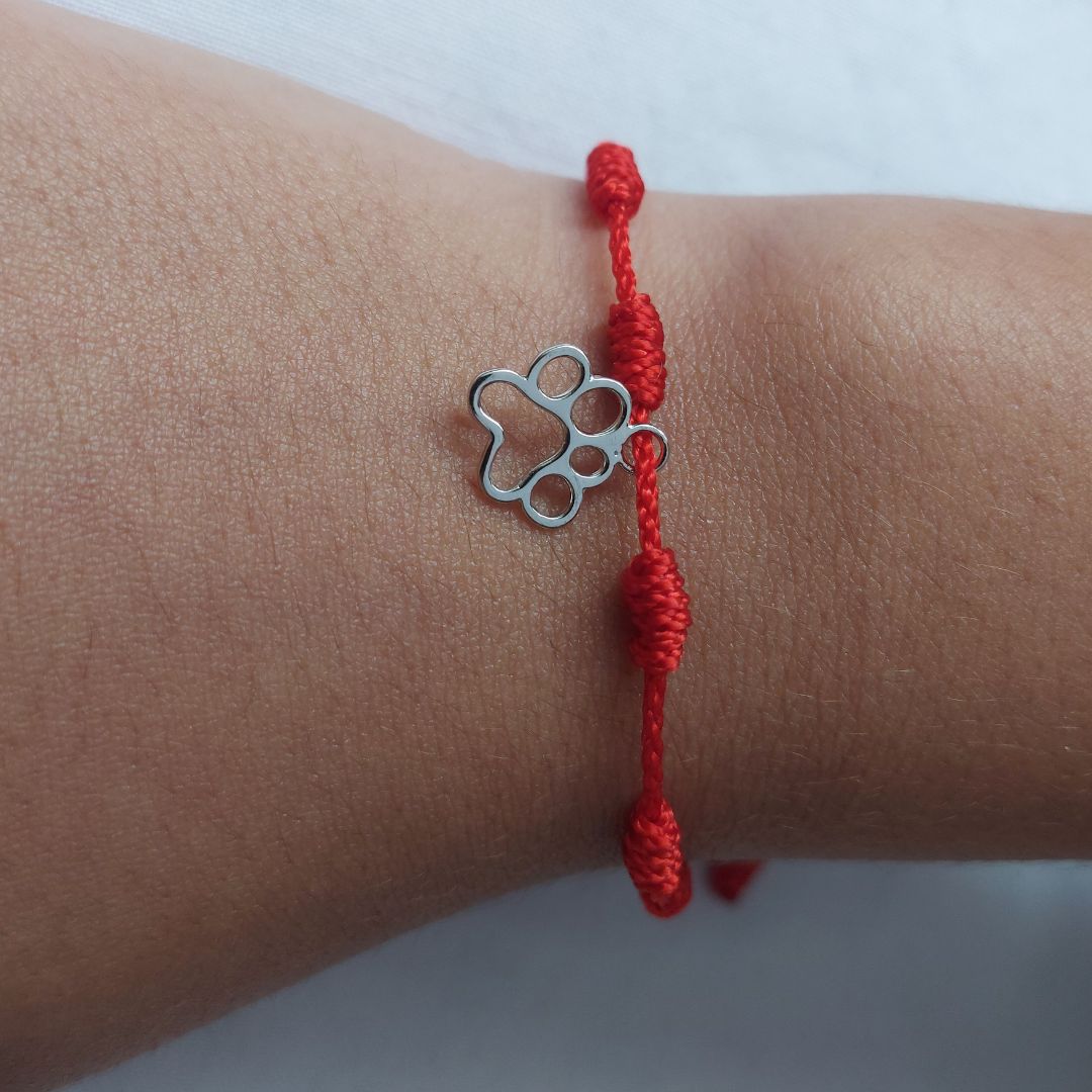 En la muñeca lleva una pulsera de hilo roja con 7 nudos, conocidas como pulseras de la suerte, con un charm de huella de pandora