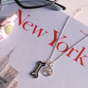 Collar para niñas con colgantes de huella y hueso en plata de Tous, sobre un libro de nueva york 
