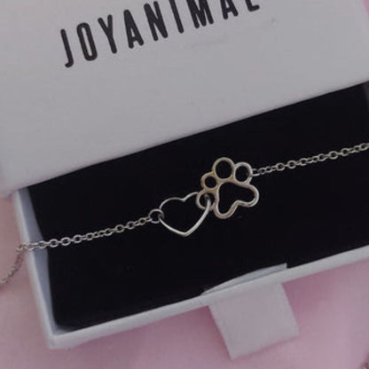 Colgante con forma de corazón y huella canina o felina entrelazados, dentro de una caja de regalo con lazo de singularu
