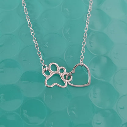 Collar con huellita y corazón en plata de ley, sobre una tela color turquesa del corte ingés