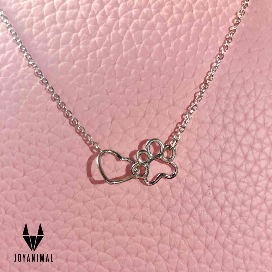 Collar con una huella y un corazón de plata de ley by Pandora, sobre una tela rosa