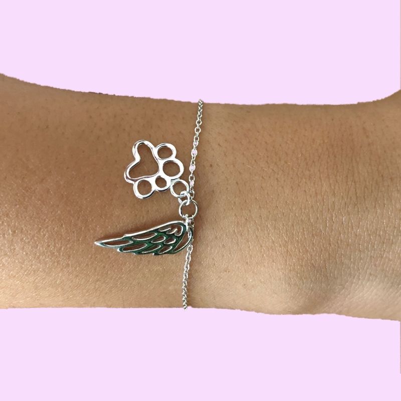 Pulsera de plata sobre muñeca de mujer, con colgantes de una huella y un ala que representan al ángel de tu perro o gata, de plata, by Pandora.